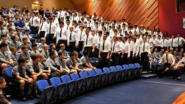 Estudiantes de la Otago Boys' High School están sentados en sillas azules en una sala con revestimiento de madera.
