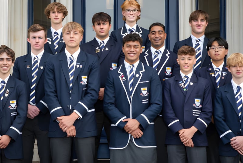 Un grupo de estudiantes está frente al edificio de la Otago Boys' High School con grandes ventanas.
