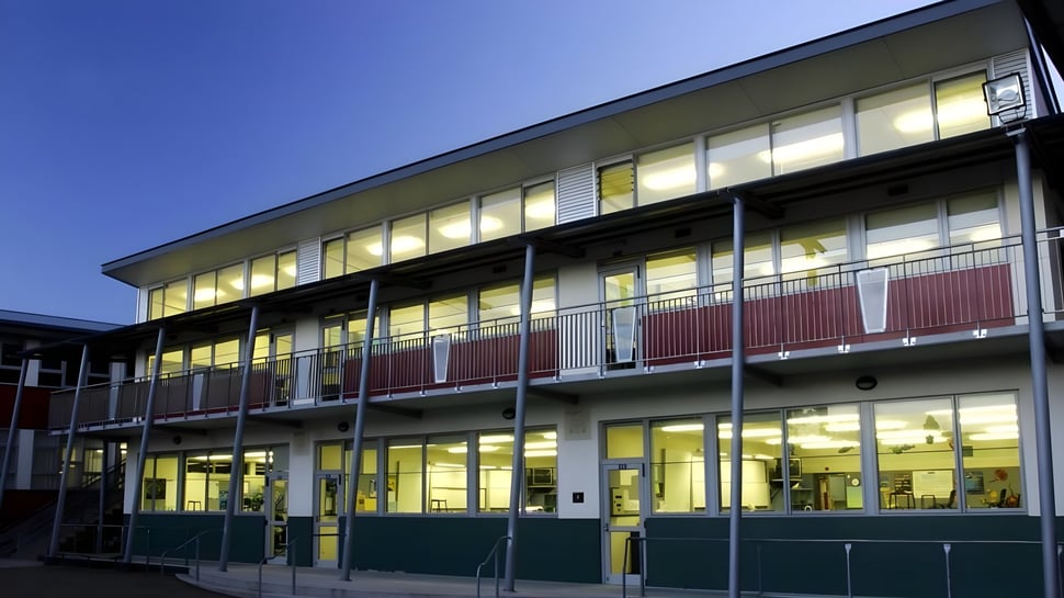 El edificio de varios pisos del Otumoetai College con grandes ventanas y un zócalo verde frente a un cielo azul.