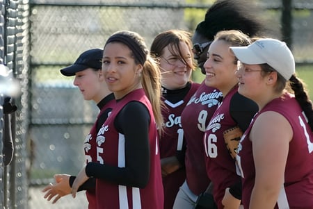 Un grupo de jóvenes atletas está reunido en el campo deportivo de Our Savior New American School cerca de una cerca de alambre.