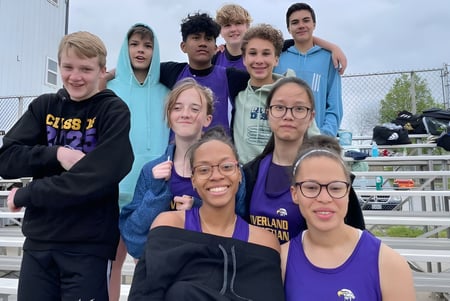 Un grupo de estudiantes de las Overland Christian Schools sonríe al aire libre frente a una cerca y gradas.