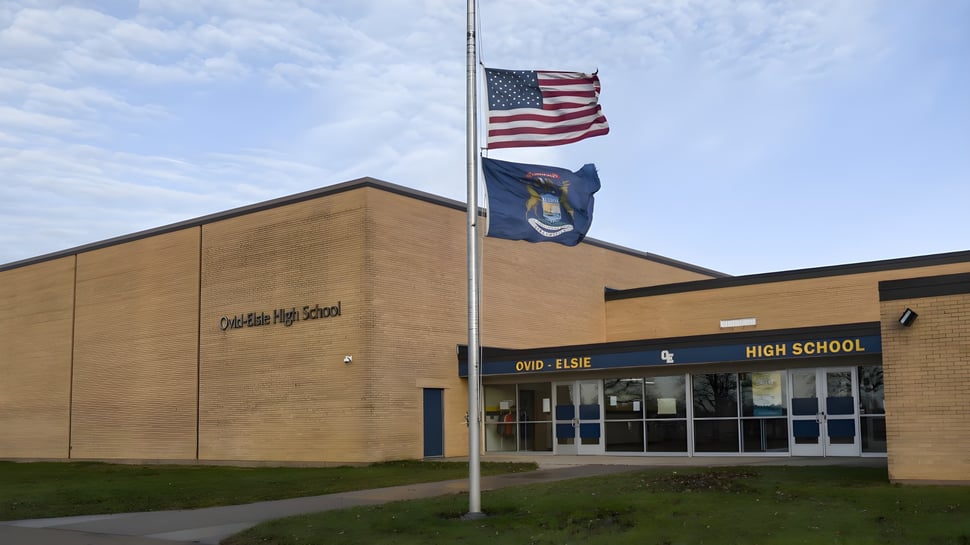 El edificio de la Ovid-Elsie High School con bandera americana y estatal en un asta de bandera en primer plano.