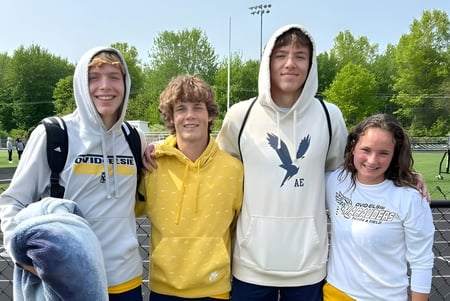 Cuatro estudiantes de la Ovid-Elsie High School están juntos en un campo deportivo al aire libre.
