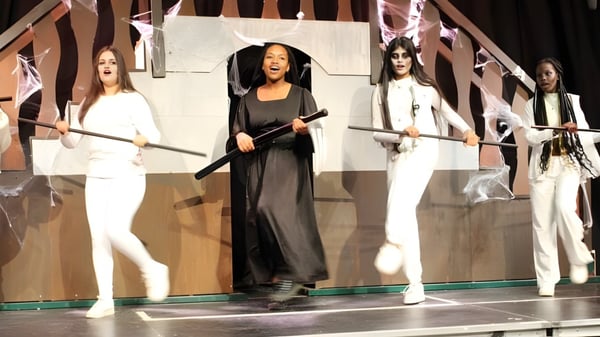 Un grupo de mujeres está en el escenario de la Oxford Academy frente a un fondo geométrico.
