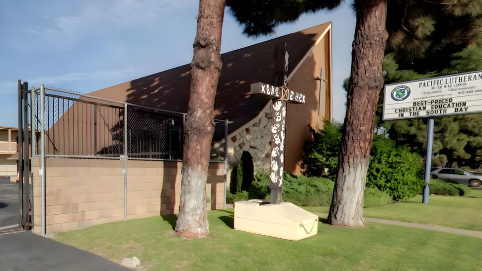 El moderno edificio de la Pacific Lutheran High School con techo triangular se encuentra en un área cubierta de hierba con altas palmeras.