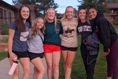 Un grupo de estudiantes está afuera en un prado con árboles de fondo en el campus de la Pacific Lutheran High School.