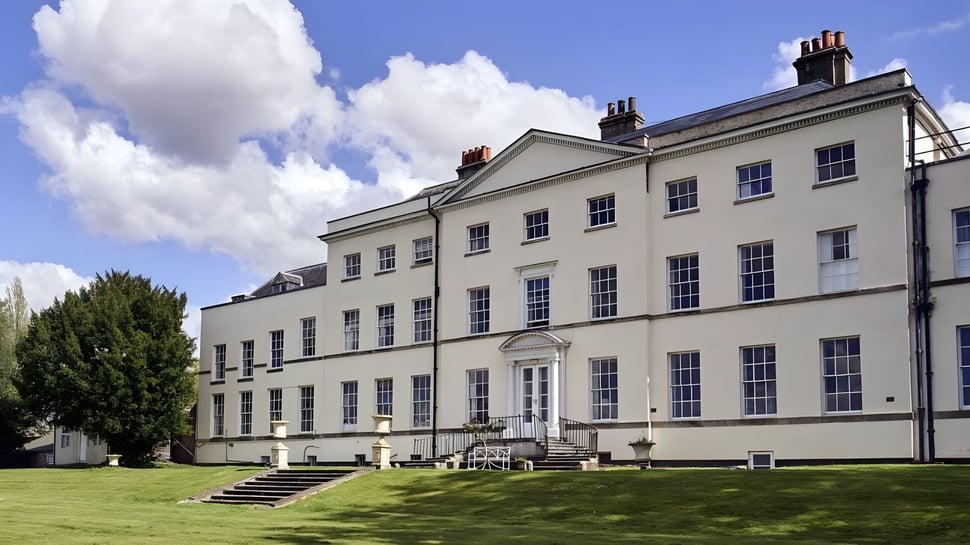 El edificio principal de varios pisos de Padworth College está rodeado de césped bien cuidado y vegetación verde bajo un cielo nublado.