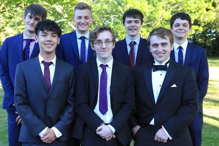 Un grupo de estudiantes del Padworth College está de pie con ropa formal en un prado con árboles de fondo.