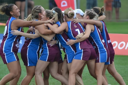 Un grupo de atletas de la Palm Beach Currumbin State High School se abraza en el campo de deportes frente a una bandera roja y blanca.
