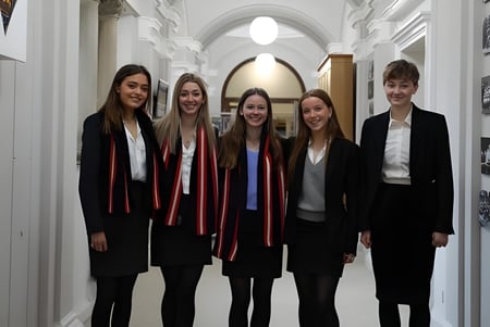 Cinco jóvenes en ropa formal están juntos en el pasillo del campus del Pangbourne College.