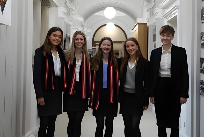 Cinco jóvenes en ropa formal están juntos en el pasillo del campus del Pangbourne College.