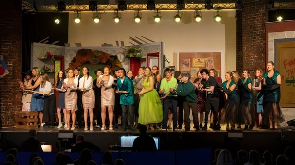 Un grupo de estudiantes de la Panorama Ridge Secondary School está vestido formalmente en un escenario frente a una pared de ladrillos.