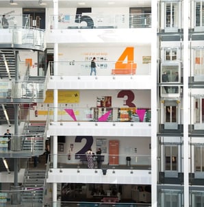 Vista interior de un edificio universitario moderno de varias plantas con estudiantes en los pasillos.
