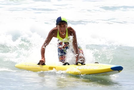 Una persona en una tabla de surf amarilla navega por las olas frente a la costa del Papamoa College.