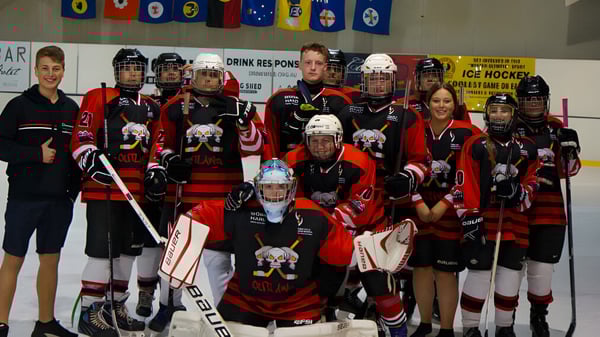 Un grupo de estudiantes de hockey de Para Hills High School posa en una pista de hielo con pancartas del equipo de fondo.