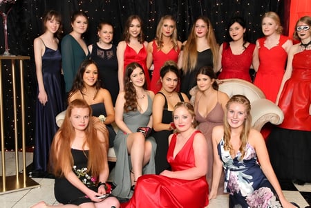 Un grupo de estudiantes de Paraparaumu College posan con vestidos formales frente a un fondo oscuro con luces brillantes.