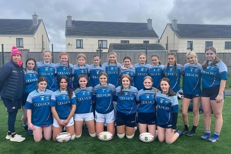 Un grupo de jóvenes futbolistas de la Patrician Presentation Secondary School posan frente a casas bajo un cielo nublado.