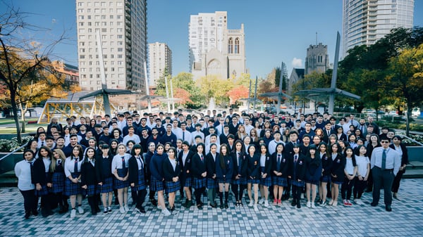 Un grupo de estudiantes de la Pattison High School se reúne frente a un paisaje urbano con altos edificios y un campanario.