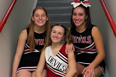 Tres alumnas de la Pemberton Secondary School en uniformes de animadoras posan juntas en la escalera.