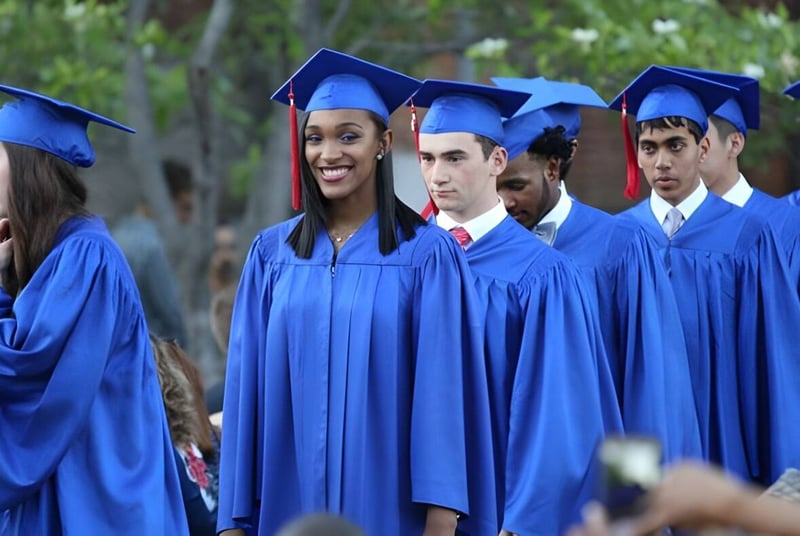 Un grupo de graduadas y graduados de la Pembroke School está de pie en togas azules sobre un campo.