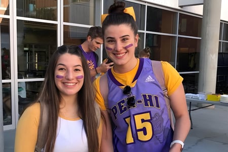 Dos estudiantes de la Penticton Secondary School están sonriendo frente a un edificio con grandes ventanas.