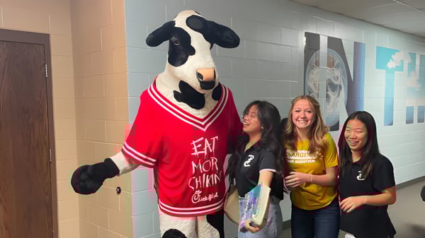 La mascota de la Peoria Christian School está con un grupo de estudiantes sonrientes en el pasillo de la escuela.