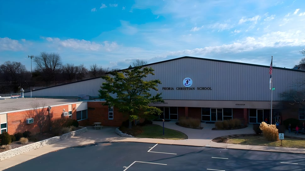 El moderno edificio escolar de la Peoria Christian School con un gran estacionamiento y árboles al fondo.