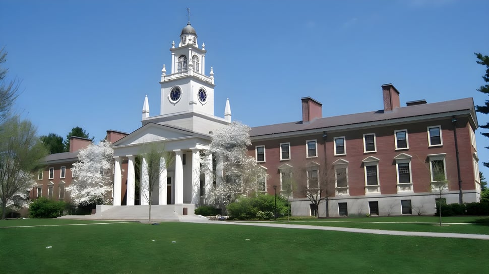 El edificio histórico con un alto reloj en el terreno de la Phillips Academy está rodeado de árboles verdes y plantas florecientes.