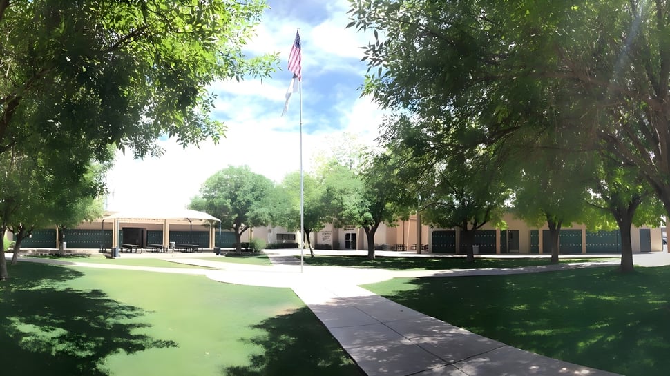 El campus de la Phoenix Christian Preparatory School muestra un camino bordeado de árboles con un edificio y la bandera americana.