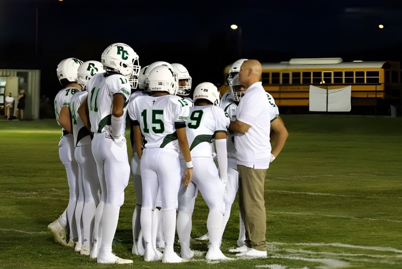 Estudiantes de la Phoenix Christian Preparatory School están juntos en camisetas blancas en un campo de fútbol débilmente iluminado con un autobús escolar al fondo.