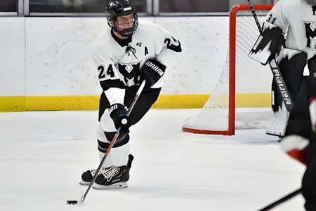 Un jugador de hockey con camiseta blanca y pantalones negros juega sobre el hielo en el terreno de la Phoenix Magnet Academy.