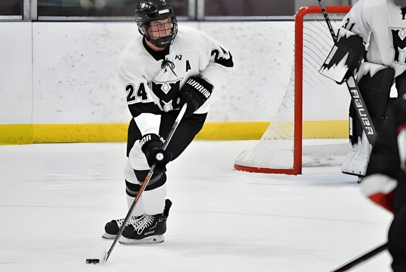 Un jugador de hockey con camiseta blanca y pantalones negros juega sobre el hielo en el terreno de la Phoenix Magnet Academy.