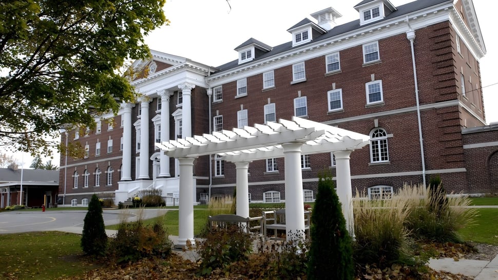 El edificio de ladrillo con fachada de columnas blancas del Pickering College está rodeado de árboles y arbustos.