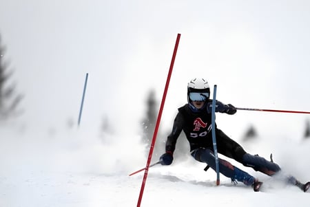 Un estudiante del Pickering College baja esquiando por una pendiente cubierta de nieve frente a pinos borrosos.