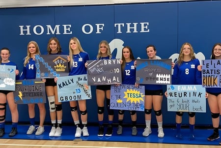 Un grupo de jugadoras de voleibol posa frente a una pared azul en el campus de la Picture Butte High School.
