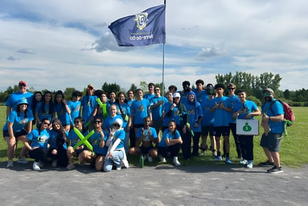 Un grupo de estudiantes con camisetas azules y verdes está frente a una bandera azul en el campus de la École secondaire publique Pierre de Blois.
