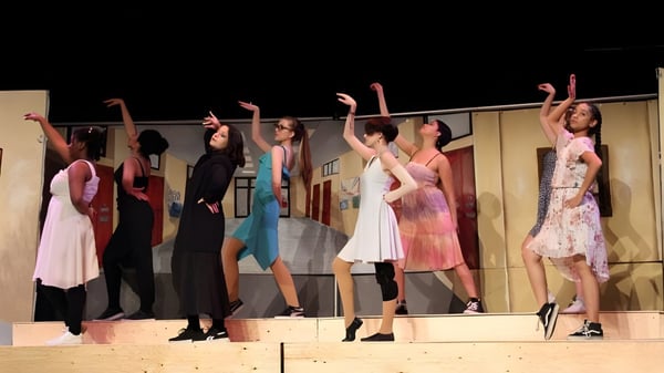 Un grupo de estudiantes de la Pierrefonds Community High School está en el escenario y levanta los brazos en una pose de baile.