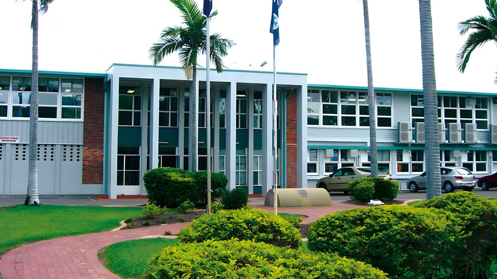 El moderno edificio de varios pisos con grandes ventanas de la Pimlico State High School está rodeado de vegetación verde con palmeras.