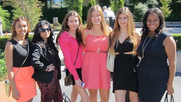 Un grupo de seis alumnas está al aire libre en el campus de la Pine Ridge Secondary School frente a un edificio y un entorno verde.