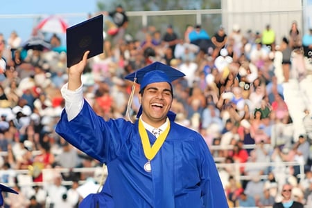 Un graduado con gorra y toga azules está frente a una multitud en la ceremonia de graduación del Placentia-Yorba Linda Unified School District.