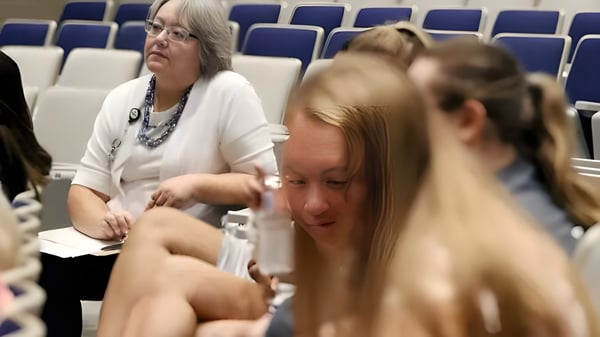 Dos mujeres están sentadas en la sala de conferencias de la Pleasant Valley Secondary School frente a filas de asientos azules.