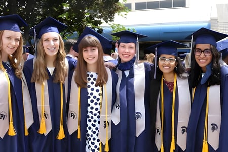 Un grupo de jóvenes mujeres en ropa de graduación está frente a un edificio universitario en el campus de la Pleasant Valley Secondary School.