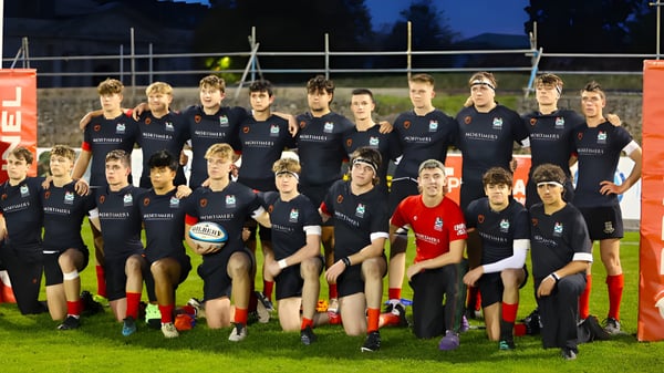 Un grupo de jóvenes atletas está en uniforme en el campo deportivo del Plymouth College de noche bajo las luces.
