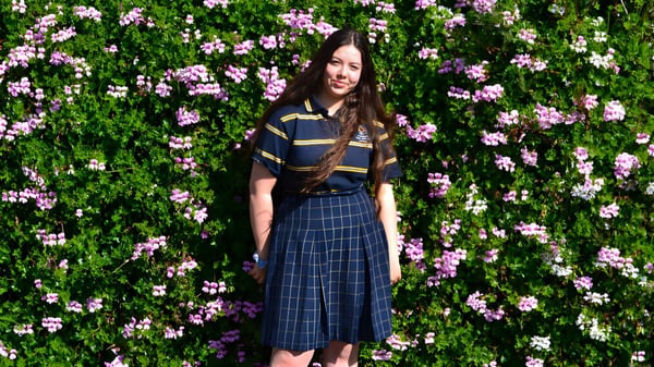 Una joven está en un jardín verde con flores rosas en el terreno del Plympton International College.
