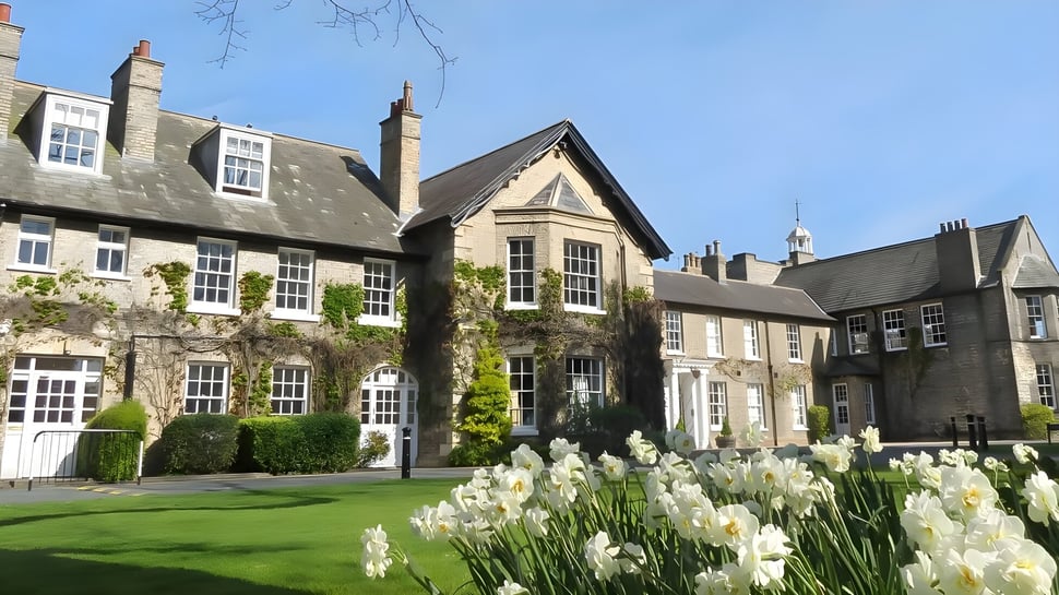 El patio de la Pocklington School muestra un cuidado césped verde y edificios de piedra históricos con narcisos blancos en primer plano.