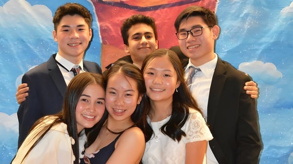 Un grupo de estudiantes de la Point Grey Secondary School posan frente a un fondo colorido con nubes.