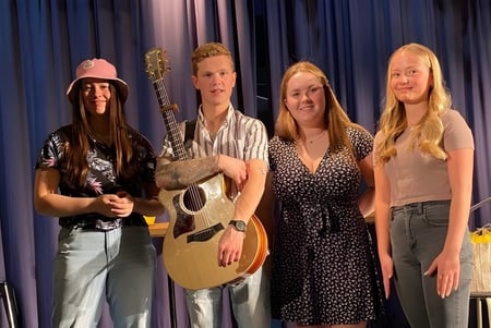 Cuatro personas, entre ellas alumnas y alumnos, están de pie como músicos en el escenario de la Polyvalente Alexandre-J.-Savoie.
