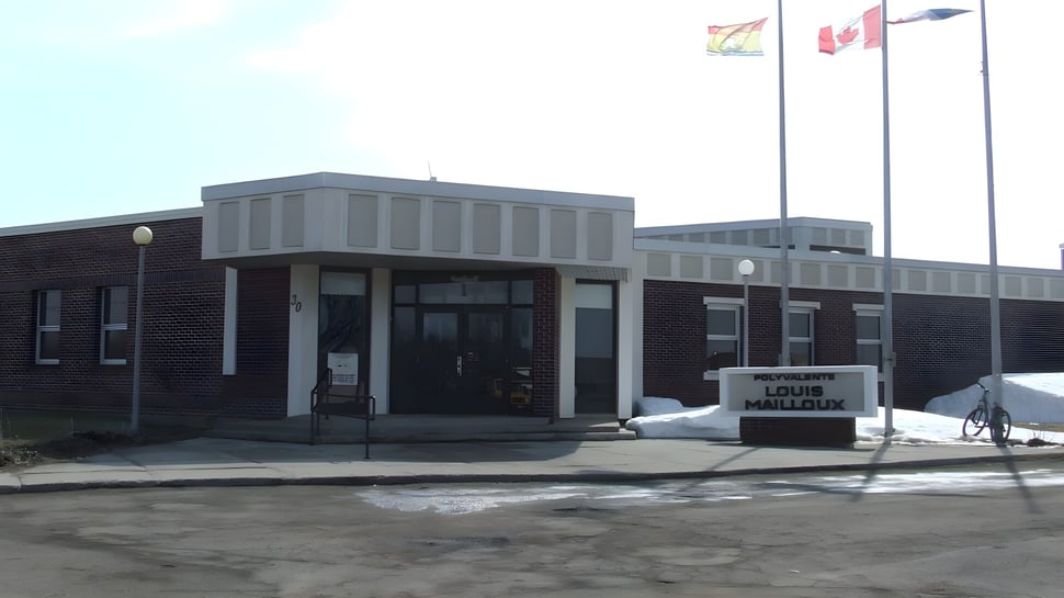 El edificio de la Polyvalente Louis-Mailloux muestra una fachada de ladrillos con un cartel y en el fondo ondean banderas.
