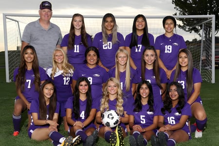 Un grupo de jóvenes futbolistas en camisetas moradas con su entrenador en el campo del Portsmouth College.