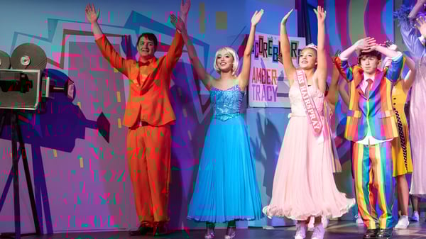 Un grupo de estudiantes del Portumna Community College se presenta en coloridos disfraces en un escenario animado.